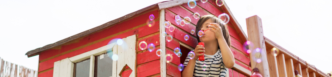 Rotes Spielholzhaus mit Junge der Seifenblasen pustet